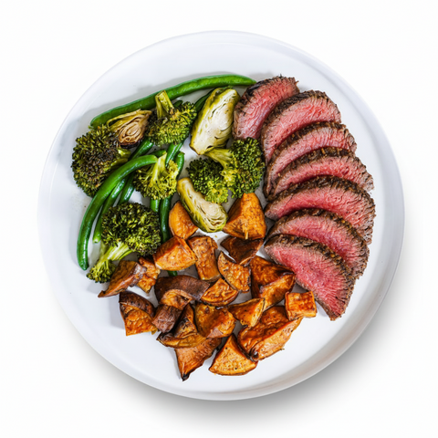 Overhead view of a roasted steak plate with sweet potatoes, broccoli, and green beans, a high-protein luxe + lemons meal
